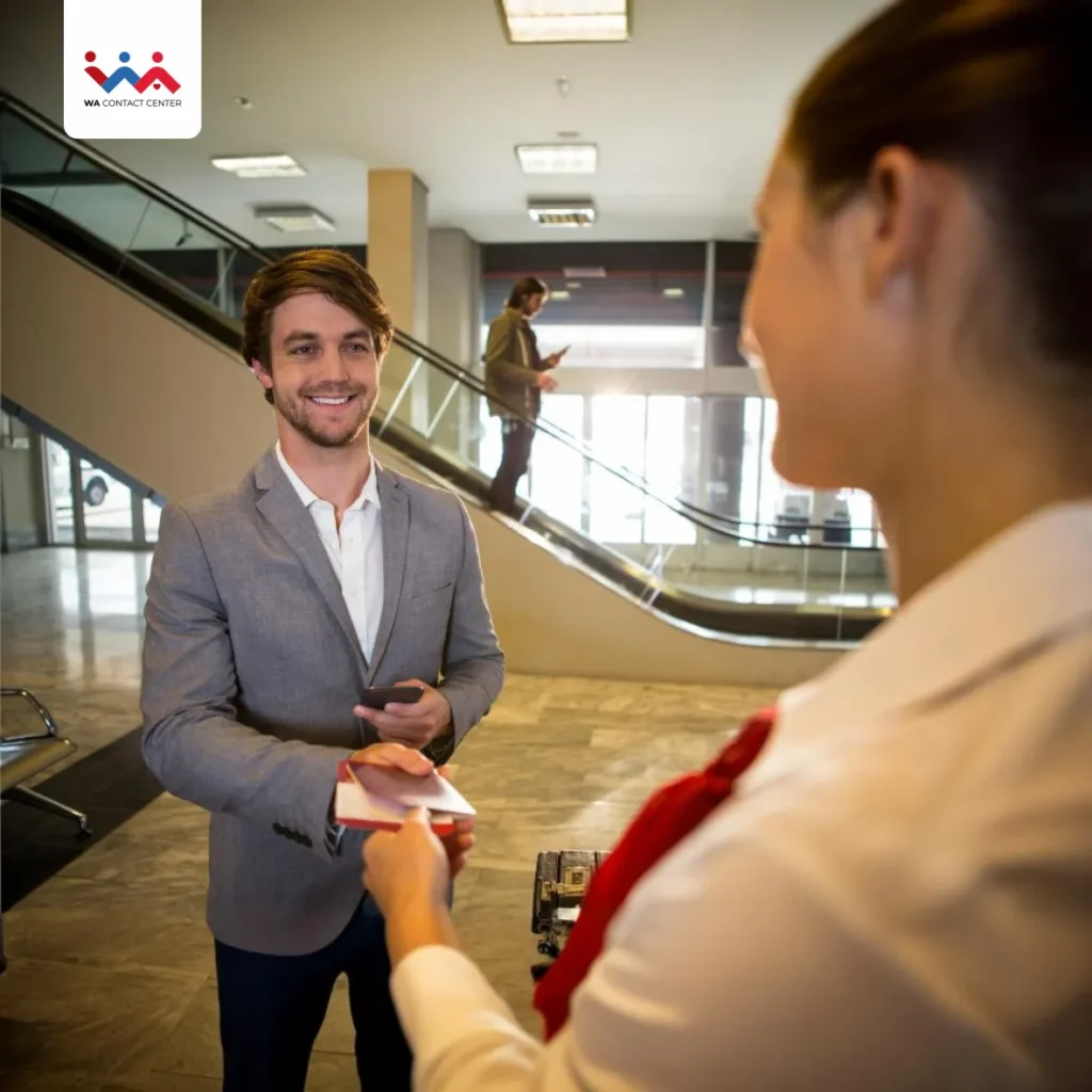 Homem de cor clara, barba e paletó, entregando o passaporte a uma agente de viagem de cor clara e uniformizada.